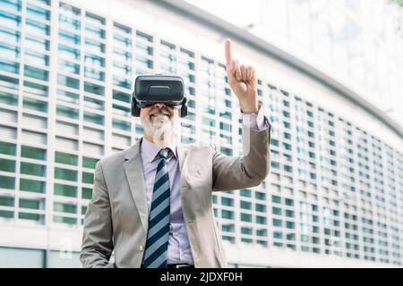 Smiling businessman wearing virtual reality simulator gesturing in front of building Stock Photo