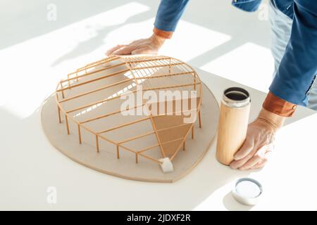 Hand of businessman holding water bottle by leaf shape wooden model on desk Stock Photo
