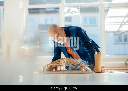 Senior architect holding water bottle analyzing leaf shape model on desk Stock Photo
