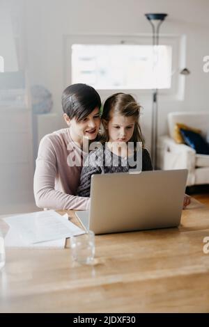 Mother and daughter watching laptop together at desk Stock Photo
