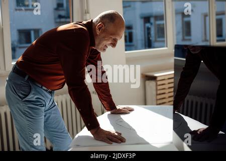 Smiling senior architect analyzing blueprint at desk Stock Photo