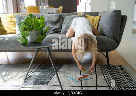 Girl picking up colored pencils from carpet at home Stock Photo