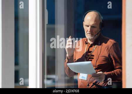 Businessman wearing headset analyzing document seen through glass Stock Photo