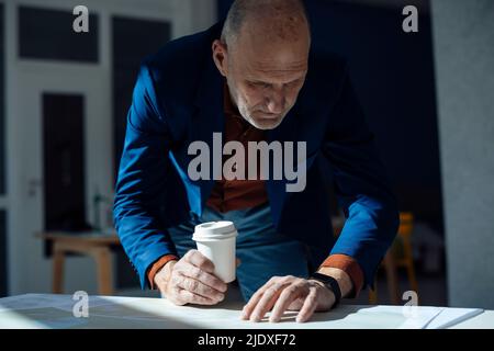 Businessman holding disposable cup checking time on smart watch at desk Stock Photo