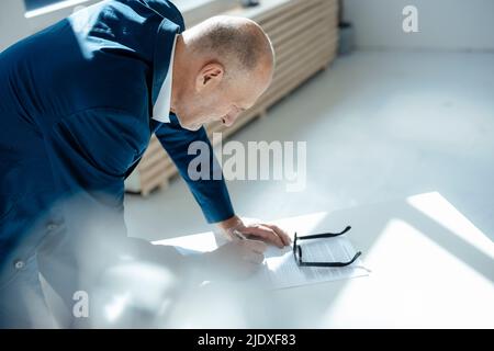 Senior businessman writing on document at desk Stock Photo