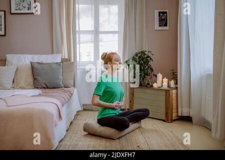 Woman sitting cross-legged practicing yoga at home Stock Photo
