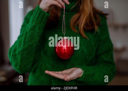 Woman wearing green sweater holding red Christmas bauble at home Stock Photo