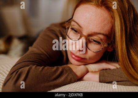 Sad woman wearing eyeglasses lying on bed at home Stock Photo