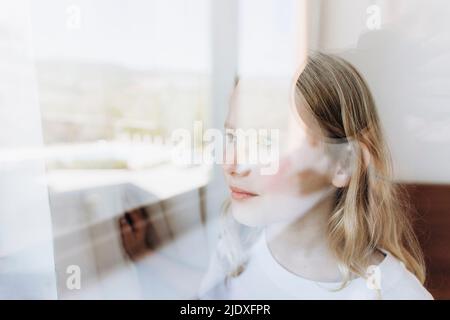 Contemplative girl looking through window Stock Photo