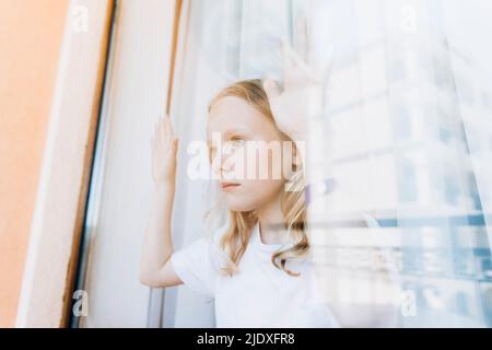 Contemplative girl looking through glass window at home Stock Photo