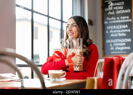 beautiful smiling woman holding wrapped Christmas present sitting in cafe Stock Photo