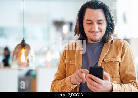 Smiling hipster man with long hair using smart phone at cafe Stock Photo