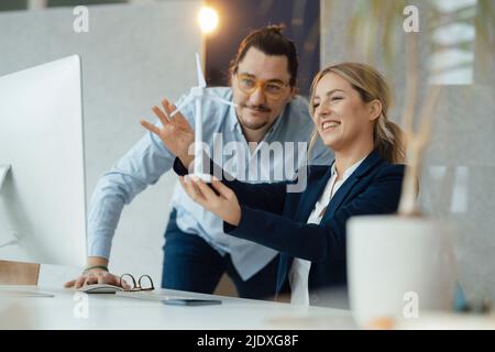 Smiling businesswoman holding wind turbine model discussing with colleague in office Stock Photo
