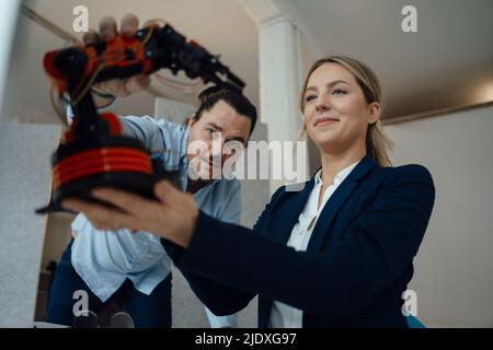Engineer discussing with colleague over robotic arm model in office Stock Photo