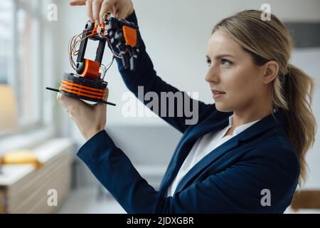 Businesswoman examining robotic arm model in office Stock Photo