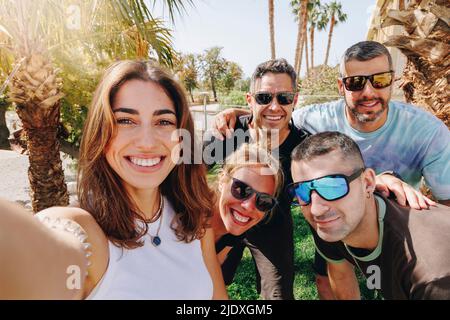 Smiling young woman taking selfie with friends on sunny day Stock Photo