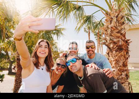 Smiling young woman with friends taking selfie through smart phone Stock Photo