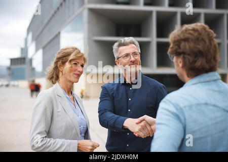 Smiling businessman shaking hand with colleague standing by businesswoman Stock Photo