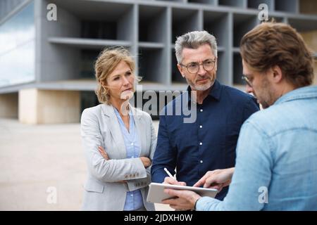 Businessman and businesswoman looking at colleague pointing on tablet PC Stock Photo