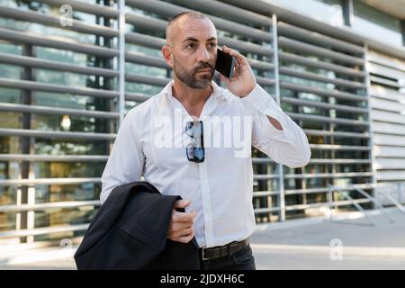 Man holding jacket talking on smart phone Stock Photo