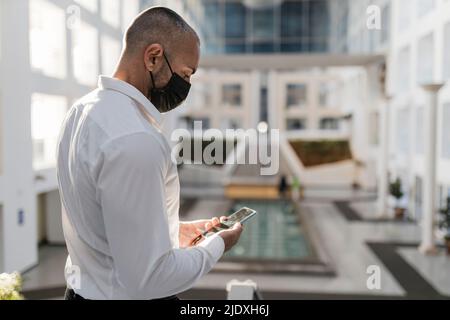 Man using smart phone wearing protective face mask Stock Photo