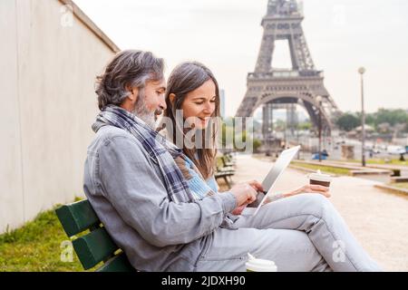 Happy woman with man using tablet PC sitting on bench near Eiffel Tower, Paris, France Stock Photo
