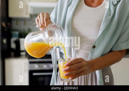 Hands of woman pouring fresh orange juice in glass from jug Stock Photo