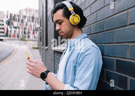 Man with headphones using smart phone near wall Stock Photo