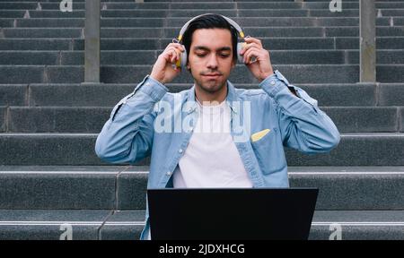 Man adjusting headphones sitting with laptop on staircase Stock Photo
