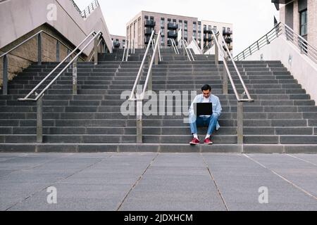 Man using laptop sitting on staircase Stock Photo
