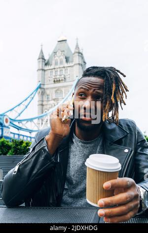 Young man with disposable cup talking on smart phone, London, England Stock Photo