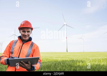 Smiling mature engineer with tablet PC standing on field Stock Photo