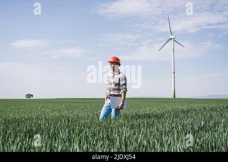 Engineer wearing hardhat holding tablet PC standing amidst wheat crops on field Stock Photo