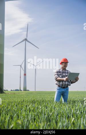 Mature engineer using digital tablet PC standing near wind turbine Stock Photo
