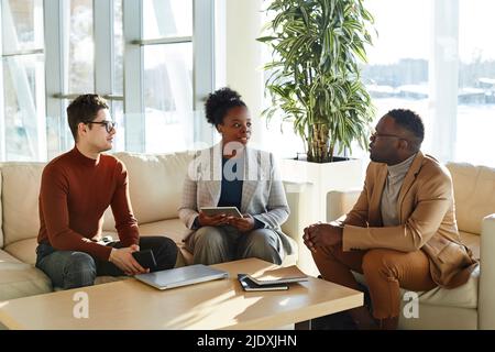 Multiracial business colleagues sitting on sofa discussing strategy in office Stock Photo