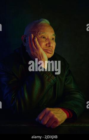 Pensive senior man sitting with hand on chin against black background Stock Photo