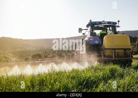 Young farmer spraying fertilizer through sprayer on tractor on field Stock Photo