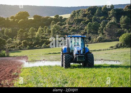 Young farmer sitting in tractor spraying fertilizer on field Stock Photo