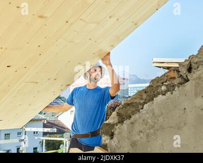 Young man working at construction site on rooftop of house Stock Photo