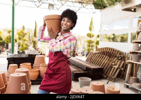 Smiling gardener carrying pot standing in warehouse Stock Photo