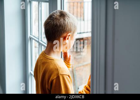 Boy looking through window at home Stock Photo