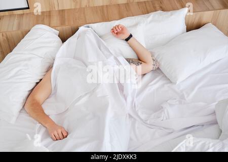 Young man sleeping under blanket in bed at home Stock Photo
