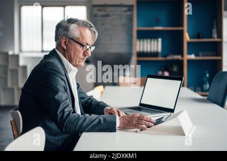 Businessman using tablet PC by laptop on desk at office Stock Photo