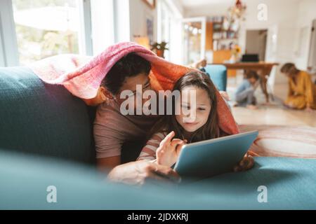 Girl using tablet PC lying with father on sofa at home Stock Photo