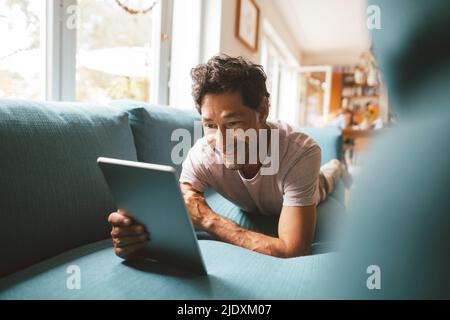 Happy man using tablet PC on sofa at home Stock Photo