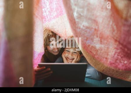 Happy mother and son using tablet PC under blanket Stock Photo