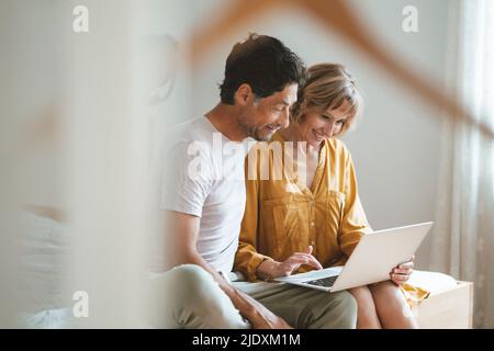 Happy woman using laptop sitting by man at home Stock Photo