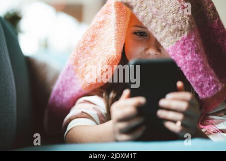 Girl using smart phone lying under blanket at home Stock Photo