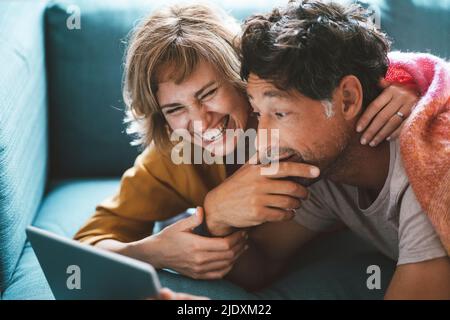 Happy mature woman lying with man using digital tablet on sofa at home Stock Photo