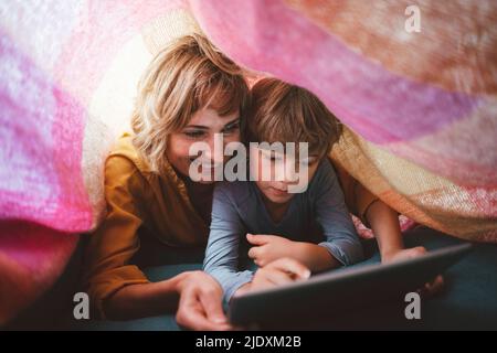 Cute boy with mother using tablet PC under blanket Stock Photo